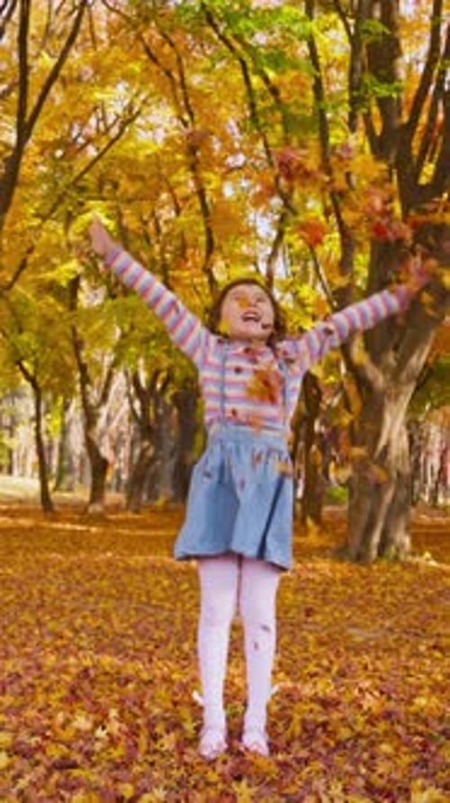 Joyful child throws pile of colorful autumn leaves in the air in autumn park