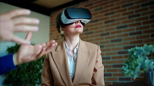 Woman impressed while using a Virtual Reality headset in an office, man hands gesturing