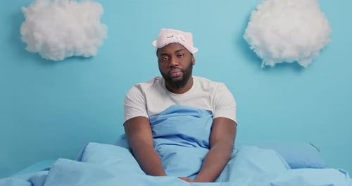 Man Sits in Bed Looking Sleepy and Yawning