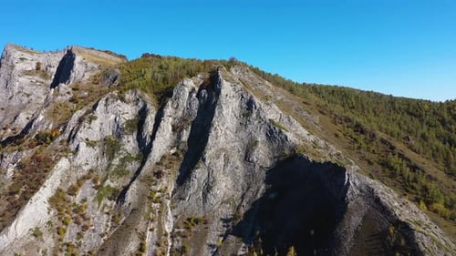 Flying above sunny autumn alpine mountain cliffs and colorful forest by drone