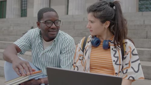 Young College Friends Sitting on Stairs with Laptop and Talking