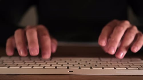 Nahaufnahme beim Tippen der Finger auf der Tastatur im dunklen Raum. Konzentrierte und entschlossene Arbeit der Frau