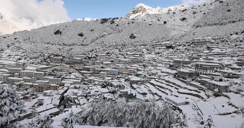 Slow pan over Namche Bazaar in the early morning with snow covered buildings.