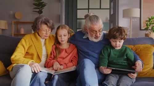 Grandparents Reading with Grandchildren on Sofa