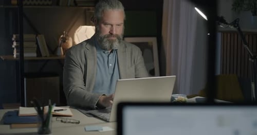 Mature Entrepreneur Working From Home Typing with Laptop Concentrated on Ecommerce in Evening