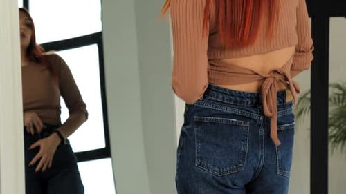 Woman wearing brown top and jeans in front of mirror