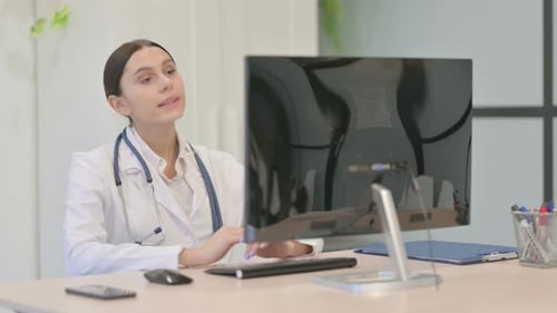Young Female Doctor Talking on Video Call on Desktop Computer in Clinic
