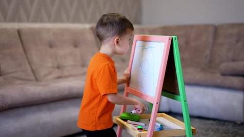 Ein entzückender kleiner Junge zeichnet mit einem blauen Marker auf das Whiteboard.