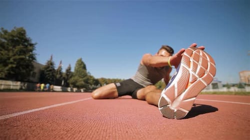 Focused Male Athlete Stretches His Leg on the Vibrant Stadium Track