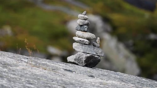 A carefully balanced stack of rocks rests on a smooth stone surface, surrounded by a natural outdoor