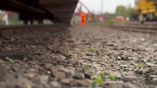 Imagem aproximada de uma alavanca ferroviária na via férrea com trabalhadores desfocados ao fundo, durante o dia