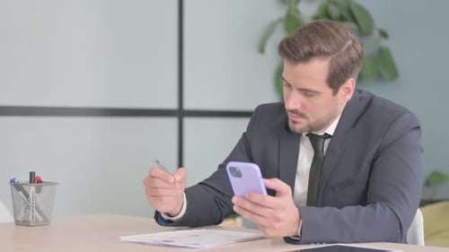 Adult Using Smartphone and Writing at Desk