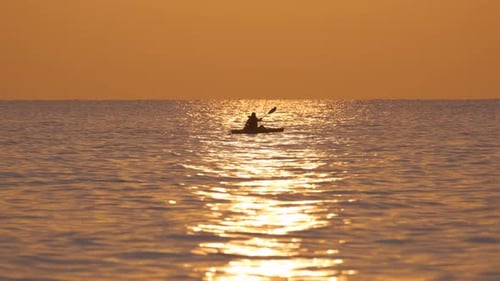 Dark Silhouette of Lonely Fisherman Rowing on His Boat on Sea Water at Sunset