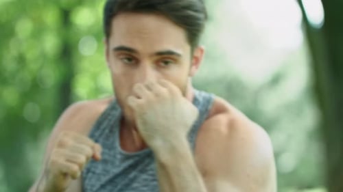 Young kickboxer training powerful punch at outdoor workout in summer park