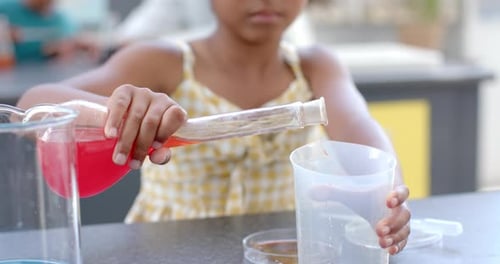 In a school classroom setting, a young biracial girl conducts a science experiment