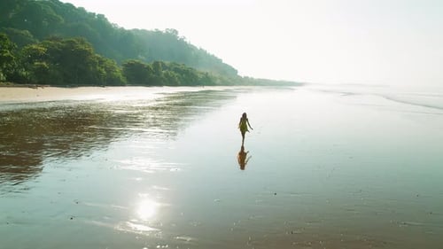 Woman in dress walks on reflective wet sand at Playa Hermosa beach Costa Rica