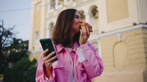 Woman Enjoys Croissant and Phone in Urban Setting