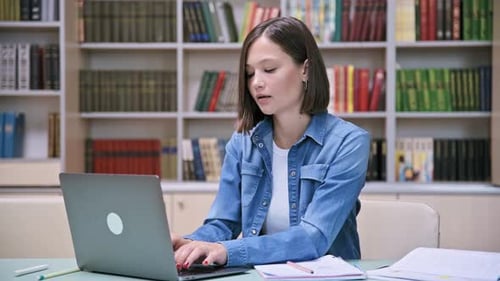 Jeune étudiante universitaire étudiant dans une bibliothèque en tapant sur un ordinateur portable