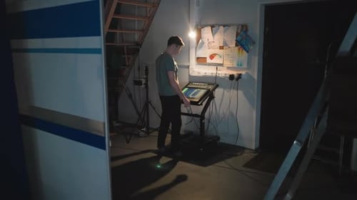 Man Working at Touchscreen Control Panel in Dim Studio Under Staircase