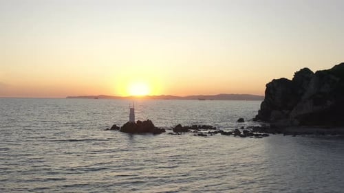 Voe sobre o pequeno farol branco, de pé sobre as rochas do mar perto de um grande penhasco íngreme no sol