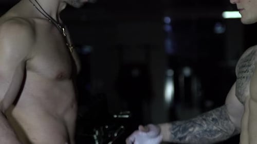 Muscular Men Clasping Hands in Dark Gym