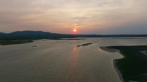 Aerial Shot of Serene Sunset Over a Tranquil Lake with Surrounding Greenery