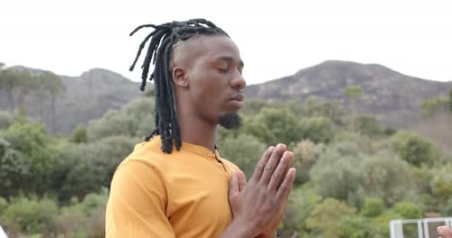 After reaching terrace by railing, African American man bowing palms at chest practicing breathing