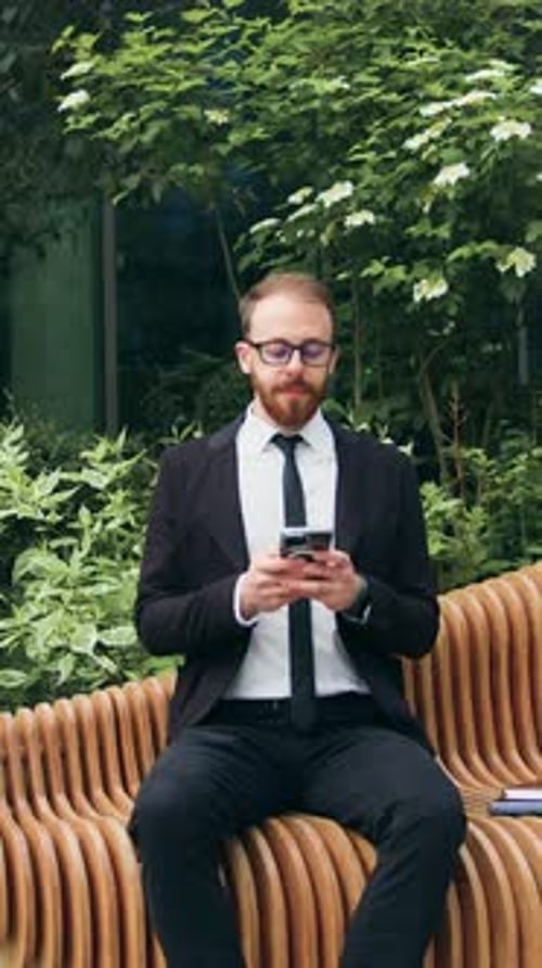 Handsome Bearded Man Using Typing Mobile Phone Sitting on Bench on City Street Attractive