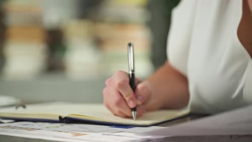Closeup of a Woman's Hand Making a Note in a Notebook in the Office
