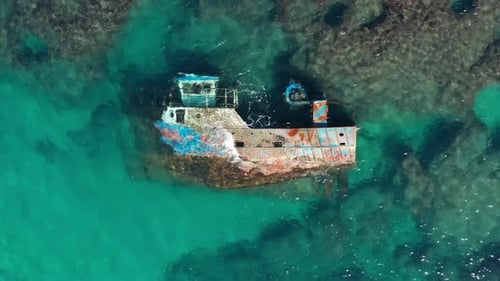 Fischerboot Schiffbruch ruht auf ihrer Seite, umgeben von seichtem Meerwasser und Felsen