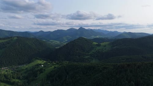 Aerial View of Green Mountain Valley with Forest Hills and Distant Peaks Under Clouds