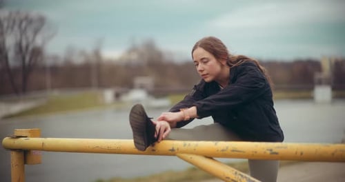 Sportswoman Stretching Legs on Bar in Park