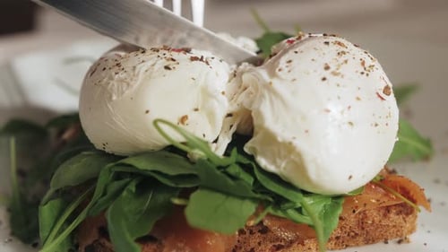 Sandwich with Smoked Salmon Arugula and Poached Egg The Client's Hands Cut an Egg with a Knife the