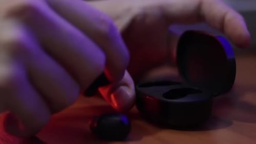 Caucasian hands in close up, place a pair of wireless earphones in their charging case which is on a