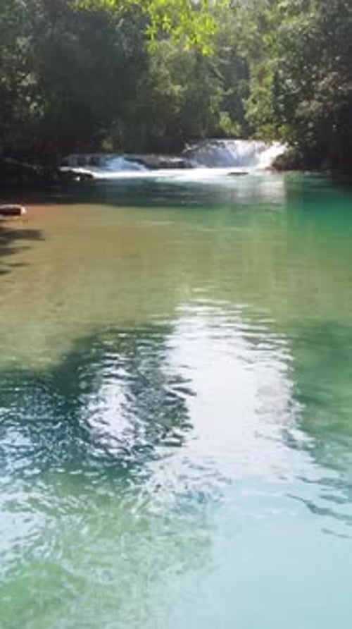 Aerial drone view of clear turquoise natural pool and small waterfall flowing through tropical jungl