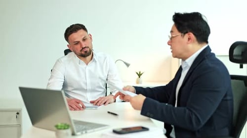 Businessmen Discussing Paperwork and Using Laptop in Modern Office