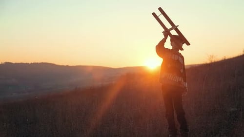 Boy Playing with Airplane on Hill at Sunset