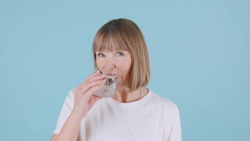 Woman Drinking Water from Glass on Blue