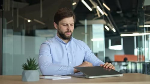 Man Closes Laptop and Leans Back, Relaxing at Desk