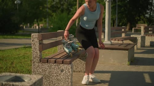 Young Lady Placing Roller Skates on Wooden Park Bench in Sunny Park Setting