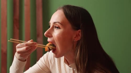 Closeup Young Brunette Woman Dressed in a Beige Sweatshirt is Sitting in Her Kitchen and Eating