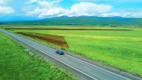 Shooting from drone shows highway among mountains of meadows. Car rushes