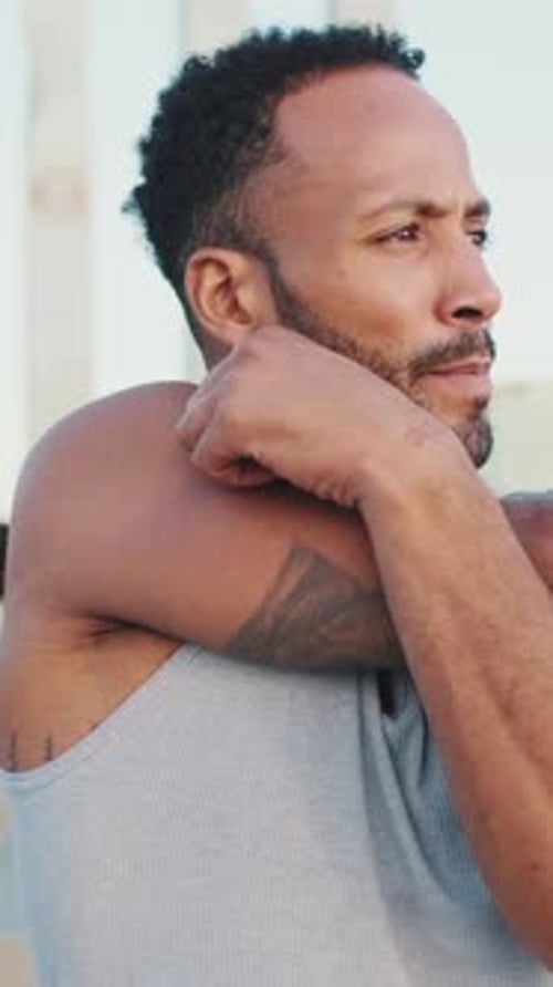 Young athlete doing warm-up, stretching his arms before training while standing on the embankment