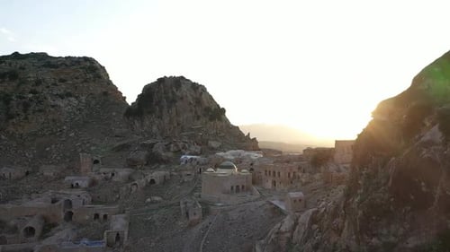 Slow aerial shot going to the left, revealing the ancient village below next to the cliffy mountain