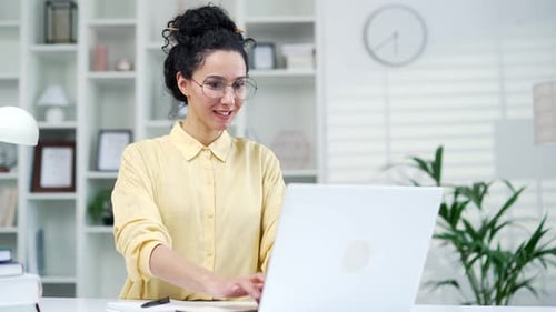 Young woman in glasses working using typing on laptop while sitting in home office. Female student s