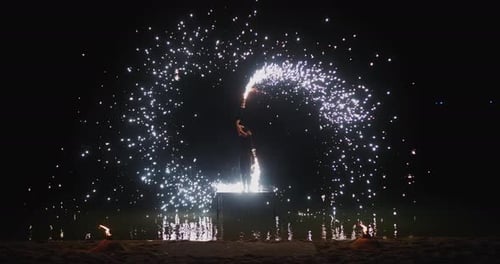 Sparks Stream From Burning Flares As Fire Dancer Performs During Fireworks on a Dark Beach Sparks