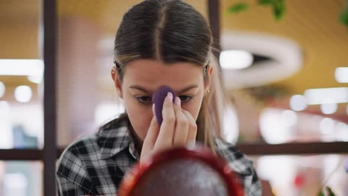 Young Woman Applying Makeup with Sponge in Mirror