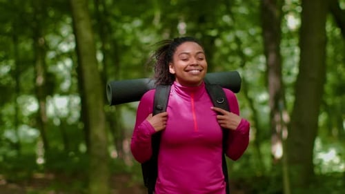 Woman With Curly Hair Carries Yoga Mat While Hiking in the Forest on a Sunny Day