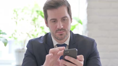 Junger Geschäftsmann surft im Büro auf Smartphone im Internet