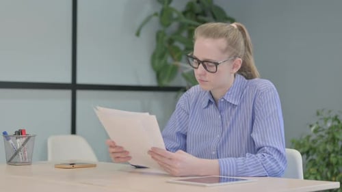 Woman Reviews Documents at Desk in Office